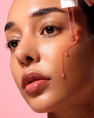 A high-impact beauty lifestyle shot featuring a close-up of a person's face being treated with a liquid skincare serum.